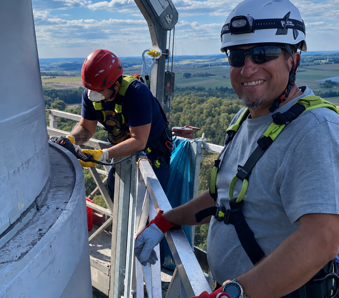 Zwei Monteure mit Schutzhelmen arbeiten an einem Anlagenturm.